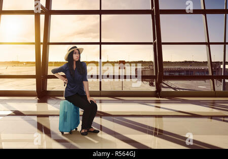 Stanchi viaggiatori asiatici donna seduta su i bagagli del volo di attesa Foto Stock
