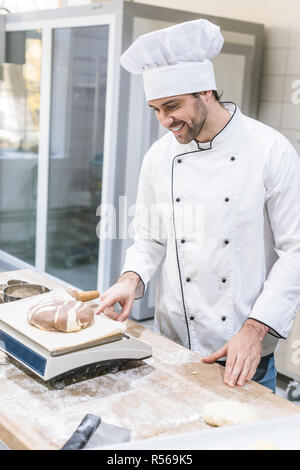 Sorridente baker del peso di pasta cruda sulla bilancia da cucina Foto Stock