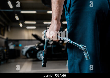 Vista parziale del meccanico automatico tenendo la chiave di manovra in officina Foto Stock