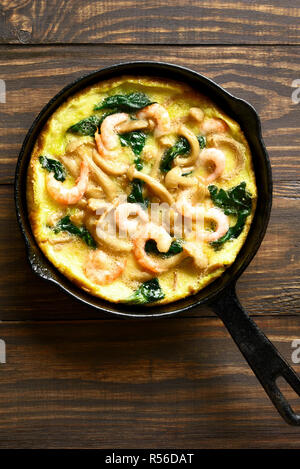 Saporiti funghi, spinaci, frittata gamberetti (uova fritte con verdure) in padella su sfondo di legno. Vista superiore, laici piatta Foto Stock