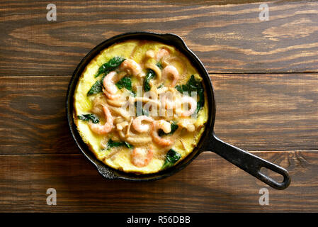 La frittata, funghi e spinaci frittata con gamberetti in padella su sfondo di legno. Vista superiore, laici piatta Foto Stock