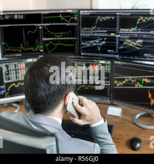 Oltre la spalla di stock broker trading online, parlando al telefono cellulare. Foto Stock