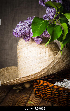 Still-life con un mazzo di lillà e un cappello di paglia, close-up Foto Stock