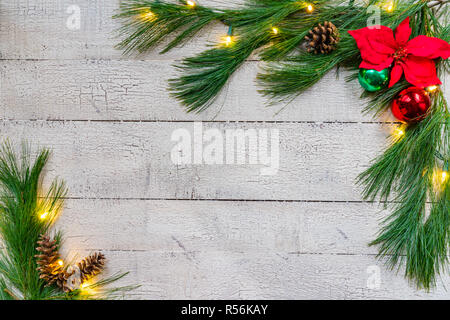 Sfondo di natale con abete rosso verdi, ornamenti e luci su weathered white tavole di pino Foto Stock