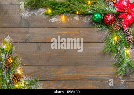 Sfondo di natale con neve, abete rosso verdi, ornamenti e luci su weathered tavole di pino Foto Stock