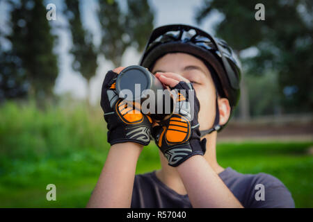 Ragazzo con il casco protettivo di bere da un nero la bottiglia di plastica Foto Stock