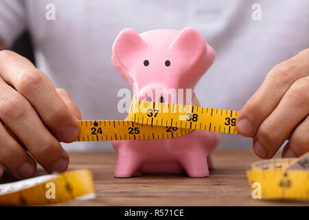 Man mano Piggybank di misura con il metro a nastro sulla scrivania in legno Foto Stock