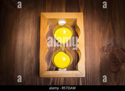 In legno sabbia retrò vetro orologio giacciono sul lato con sabbia su sfondo di legno. Tempo il concetto di arresto. Foto Stock