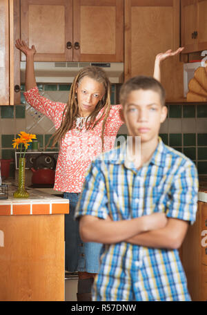 Frustrati teen sta con le braccia incrociate come sua madre getta le mani in aria Foto Stock