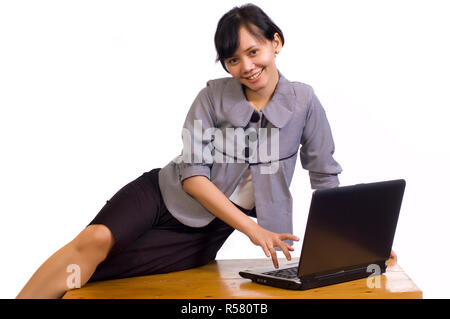 Business donna sedersi sul tavolo e sorridente con notebook Foto Stock