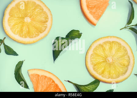 Fette di agrumi e di erbe di menta modello sul retro dello Sfondo menta dal di sopra. Vista dall'alto di arancia e di limone fette di frutta su sfondo color pastello. Foto Stock