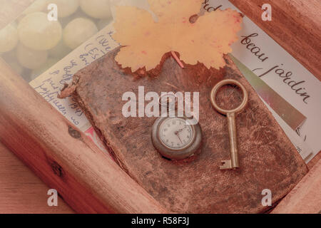 La nostalgia. Un vintage orologio da tasca, una chiave, un autunno foglia e vecchie lettere e cartoline in una scatola di legno, tonica immagine Foto Stock