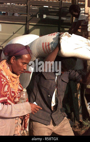 1993 - dritto sulla ripresa di un somalo uomo che porta a 50 Kg sacchetto di granturco sopra la sua testa. Egli lo porta per una donna somala che è a sinistra del telaio. Il cibo viene distribuito dagli irlandesi in rilievo la preoccupazione dell'organizzazione. Il cibo e i materiali di consumo forniti sono a diretto sostegno di Restore Hope. Foto Stock