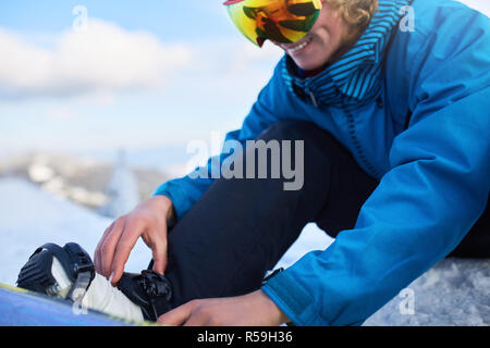 Snowboarder cinghie nelle sue gambe in scarponi da snowboard in moderno fast flow legature con cinghie. Pilota a ski resort si prepara per la sessione di freeride e . Uomo che indossa abiti alla moda. Piedi di close-up. Foto Stock