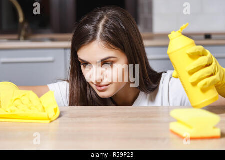 Piuttosto con i capelli lunghi ragazza in t-shirt bianco giallo da indossare guanti di gomma sfrega sulla tabella della cucina lei attentamente salviette Foto Stock