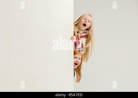 Banner con sorpresa di vedere i bambini sbirciare il bordo con copyspace. Il ritratto del piccolo grazioso ragazze ragazzi guardando la telecamera contro studio bianco parete. Moda per bambini e felice concetto emozioni Foto Stock