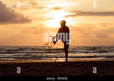 Uomo salta al tramonto sul mare Foto Stock