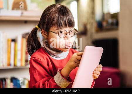 Coinvolti nel disegno. Dark-eyed sunny ragazza che mostra la sua linguetta sentirsi coinvolti nel disegno Foto Stock