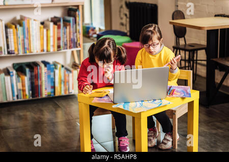 Cartoon su laptop. Due sorelle con disordine genetico guardare cartoon sul computer portatile in kindergarten Foto Stock
