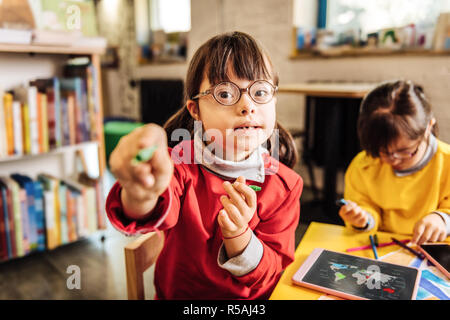 Crayon condivisione. Carino incantevole sunny bambino che condivide la sua matita verde con il suo insegnante nella scuola materna Foto Stock