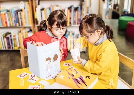 Suore a studiare. Dai capelli scuri sorelle incantevole con la sindrome di Down che studiano in inclusive kindergarten Foto Stock