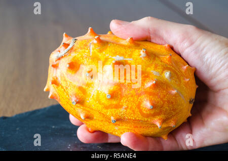 Frutta (Kivano Kiwano) melone in mano su sfondo di legno. Close up. Foto Stock