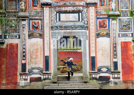 Donna della tribù di spedizione (sub-gruppo di Miao) passeggiate attraverso il tempio gateway, Feiyunya tempio, nr Kaili, Guizhou, Cina Foto Stock