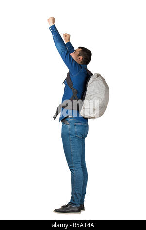 Vista laterale a piena lunghezza Ritratto di fiducioso giovane uomo che porta uno zaino sollevando in alto le mani celebrare la vincita, attività umana viaggio concetto felice Foto Stock