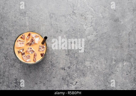 Cioccolato, vaniglia e caramello o cannella caffè ghiacciato in bicchiere con paglia nero su grigio sfondo concreto. Vista da sopra con copia spazio per il testo. Foto Stock