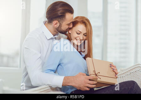 Il giovane dà un dono con i suoi occhi chiusi in camera contro la finestra. Giorno di San Valentino. Foto Stock