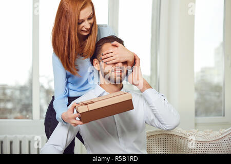 Il giovane dà un dono con i suoi occhi chiusi in camera contro la finestra. Giorno di San Valentino. Foto Stock