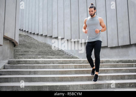 Giovane uomo jogging. Egli corre giù sui gradini. Muscoloso e ben costruito l uomo è grave e concentrata. Egli indossa uniformi sportive Foto Stock