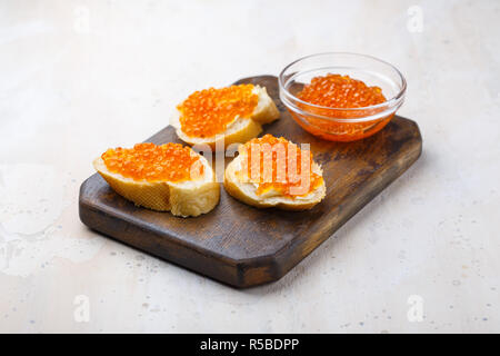 Panini con caviale rosso e il burro nella piastra su un tavolo di legno. Vista superiore Foto Stock