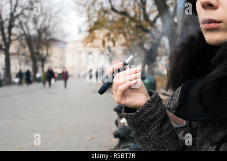 Ragazza di fumare sigaretta elettronica. Brunette donna holding Iqos Foto Stock