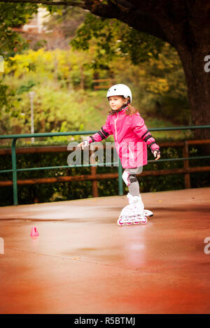 Una piccola ragazza caucasica rullo principiante in autunno nel parco la giornata piovosa. Foto Stock