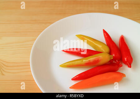Piastra del Vivid colorate a forma di peperoncino eliminabili imitazione frutti dessert servito su un tavolo di legno Foto Stock