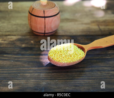 Il miglio di cereali in un cucchiaio di legno su una tavola di legno Foto Stock