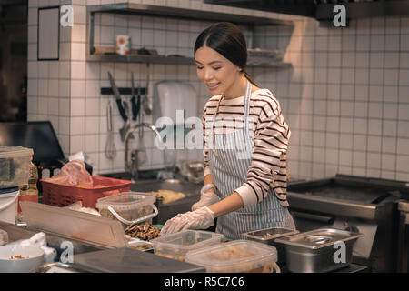 Helper di chef indossando i guanti il taglio di prodotti alimentari per insalate Foto Stock