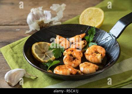 Re fritti gamberoni con aglio, limone e prezzemolo in un nero padella di ferro su un tovagliolo verde e legno rustico, messa a fuoco selezionata Foto Stock