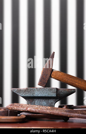 Vecchio arrugginito robusto incudine e martello e altri strumenti di fabbro su striped nero e sfondo bianco. Foto Stock