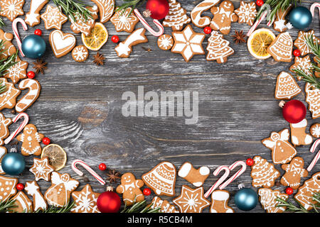 Telaio di Natale fatto di gingerbread cookies, anice stelle, bacche, candy cane lecca-lecca, palle di Natale, chip di arancio e rosmarino su sfondo di legno. Lay piatto. Foto Stock