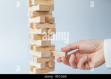 Mano d'uomo prendendo o mettere un blocco a un instabile e torre incompleta dei blocchi di legno. Concetto foto di pianificazione, tenendo conto dei rischi e la definizione di strategie. Foto Stock