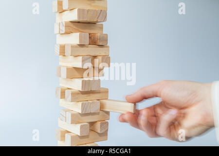 Mano d'uomo prendendo o mettere un blocco a un instabile e torre incompleta dei blocchi di legno. Concetto foto di pianificazione, tenendo conto dei rischi e la definizione di strategie. Foto Stock