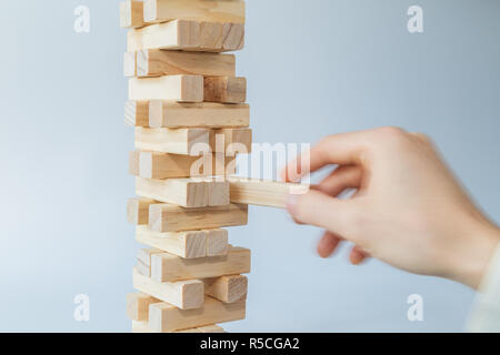 Mano d'uomo prendendo o mettere un blocco a un instabile e torre incompleta dei blocchi di legno. Concetto foto di pianificazione, tenendo conto dei rischi e la definizione di strategie. Foto Stock