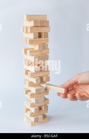 Mano d'uomo prendendo o mettere un blocco a un instabile e torre incompleta dei blocchi di legno. Concetto foto di pianificazione, tenendo conto dei rischi e la definizione di strategie. Foto Stock