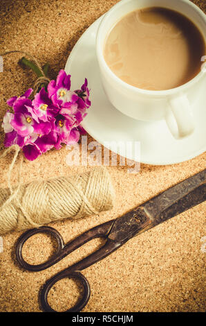 Fiori, forbici e iuta accanto alla tazza di caffè sulla bacheca di sughero. Foto Stock