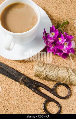 Fiori, forbici e iuta accanto alla tazza di caffè sulla bacheca di sughero. Foto Stock