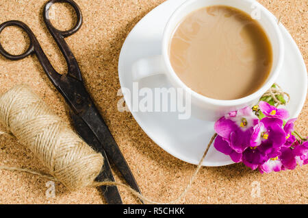 Fiori, forbici e iuta accanto alla tazza di caffè sulla bacheca di sughero. Foto Stock