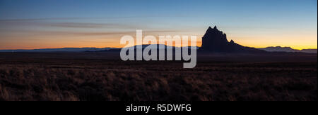 Drammatico paesaggio panoramico vista di un deserto secco con un picco di montagna in background durante una vibrante del tramonto. Prese a Shiprock, New Mexico, unite Foto Stock