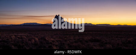 Drammatico paesaggio panoramico vista di un deserto secco con un picco di montagna in background durante una vibrante del tramonto. Prese a Shiprock, New Mexico, unite Foto Stock